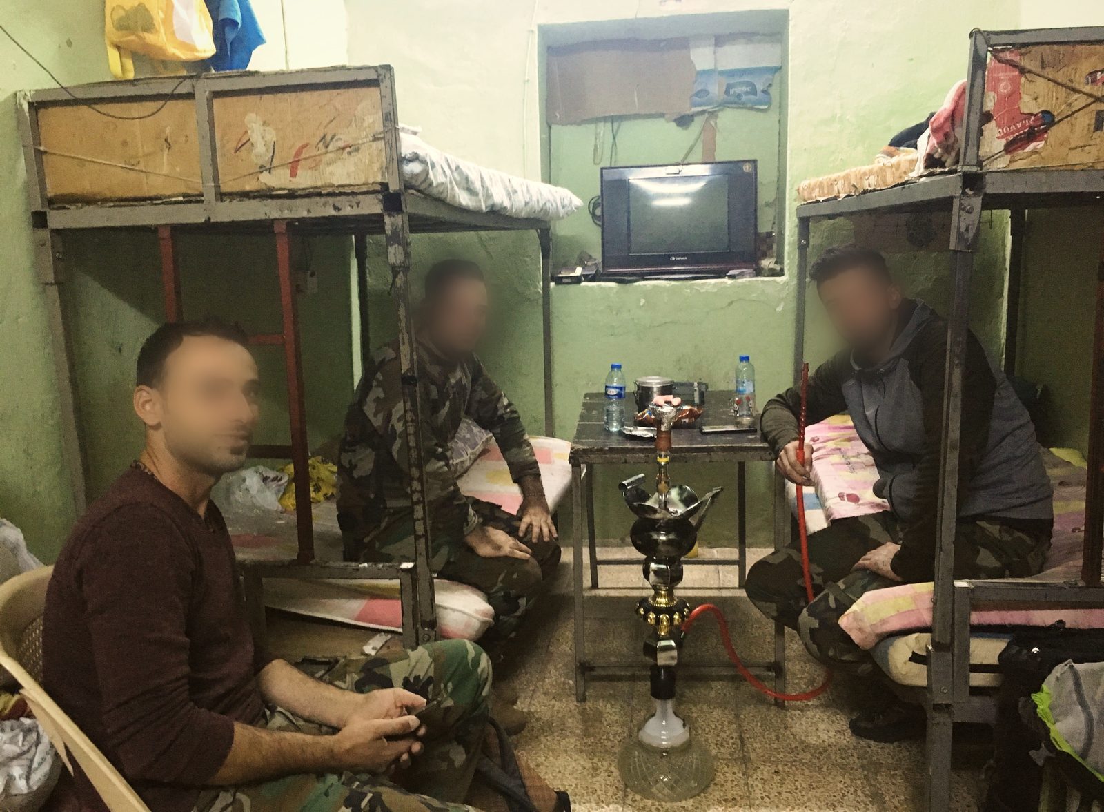 Three soldiers around a shisha between bunk beds in the small green barrack room