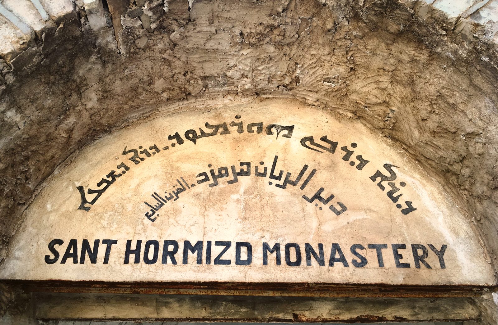 The weathered arched sign of Sant Hormizd Monastery, painted in Syriac, Arabic and English