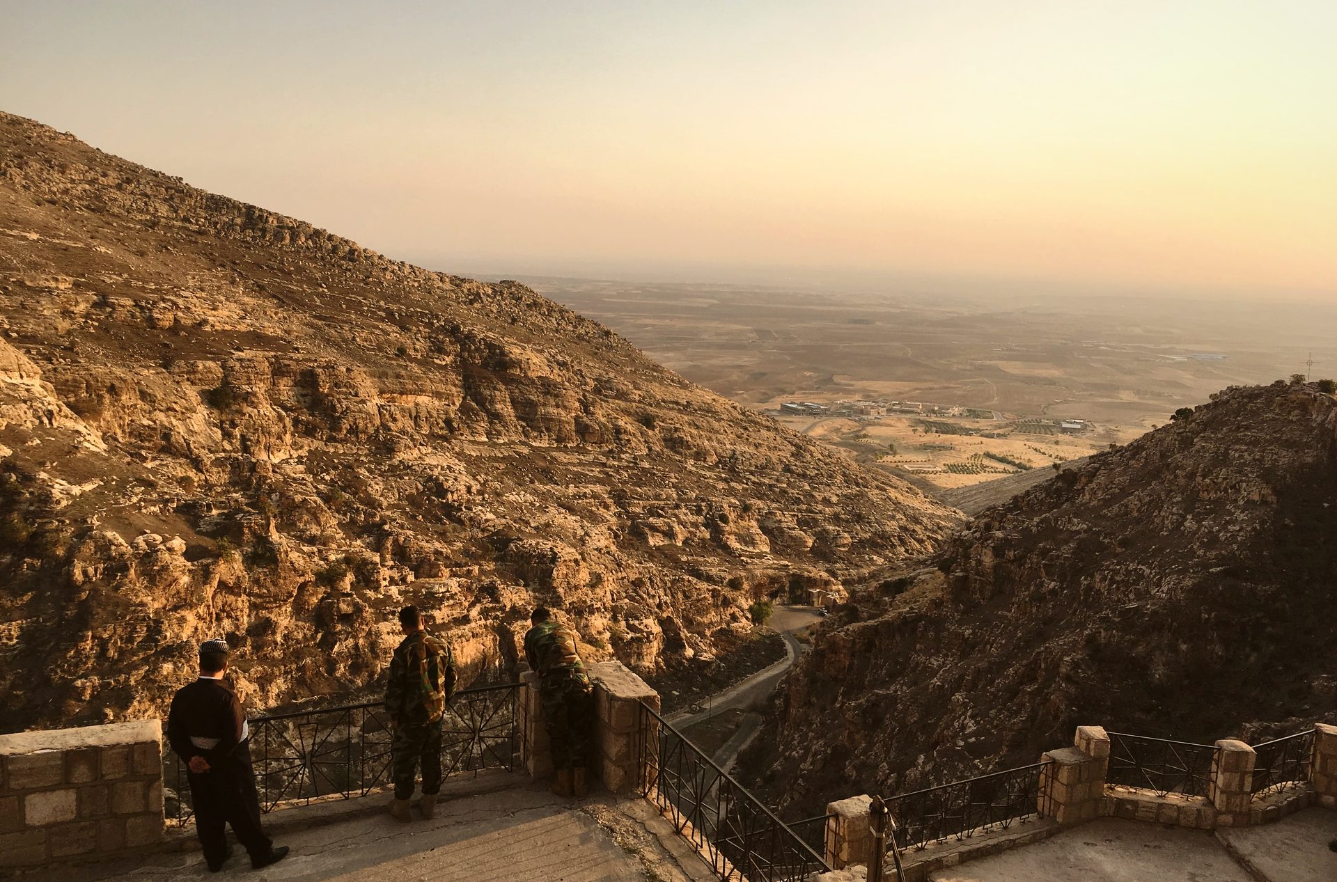 Two figures looking out from the monastery terrace over the vast Nineveh plain at dusk