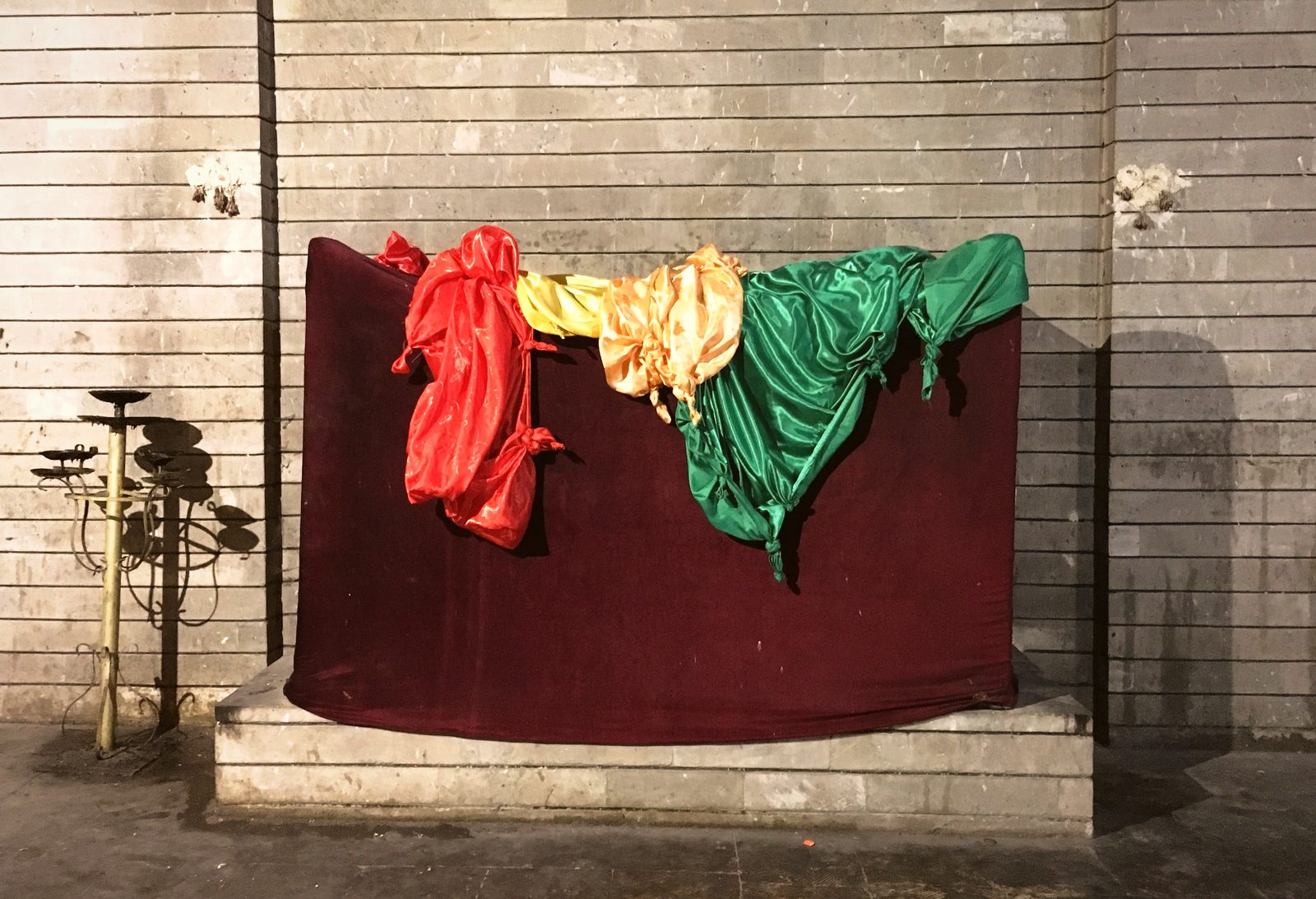 A tomb draped in deep red velvet with knotted silk cloths in red, yellow, gold and green laid across it