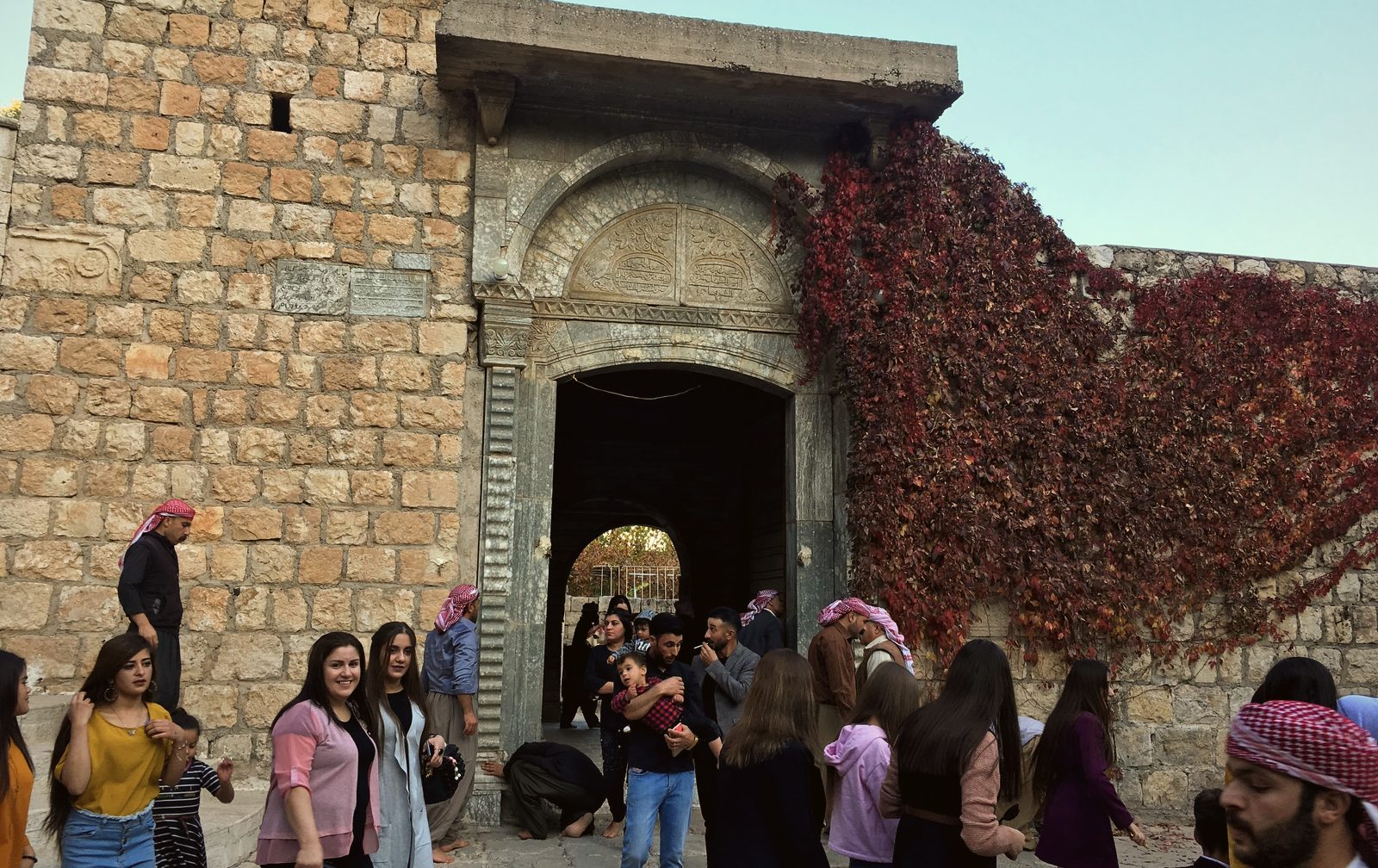 Crowds of Yazidi pilgrims in holiday clothes gathered at the ivy-covered gate of Lalish
